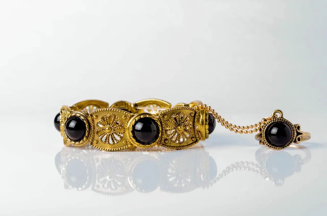 Close-up of an ornate gold bracelet with black onyx stones on a reflective white surface.